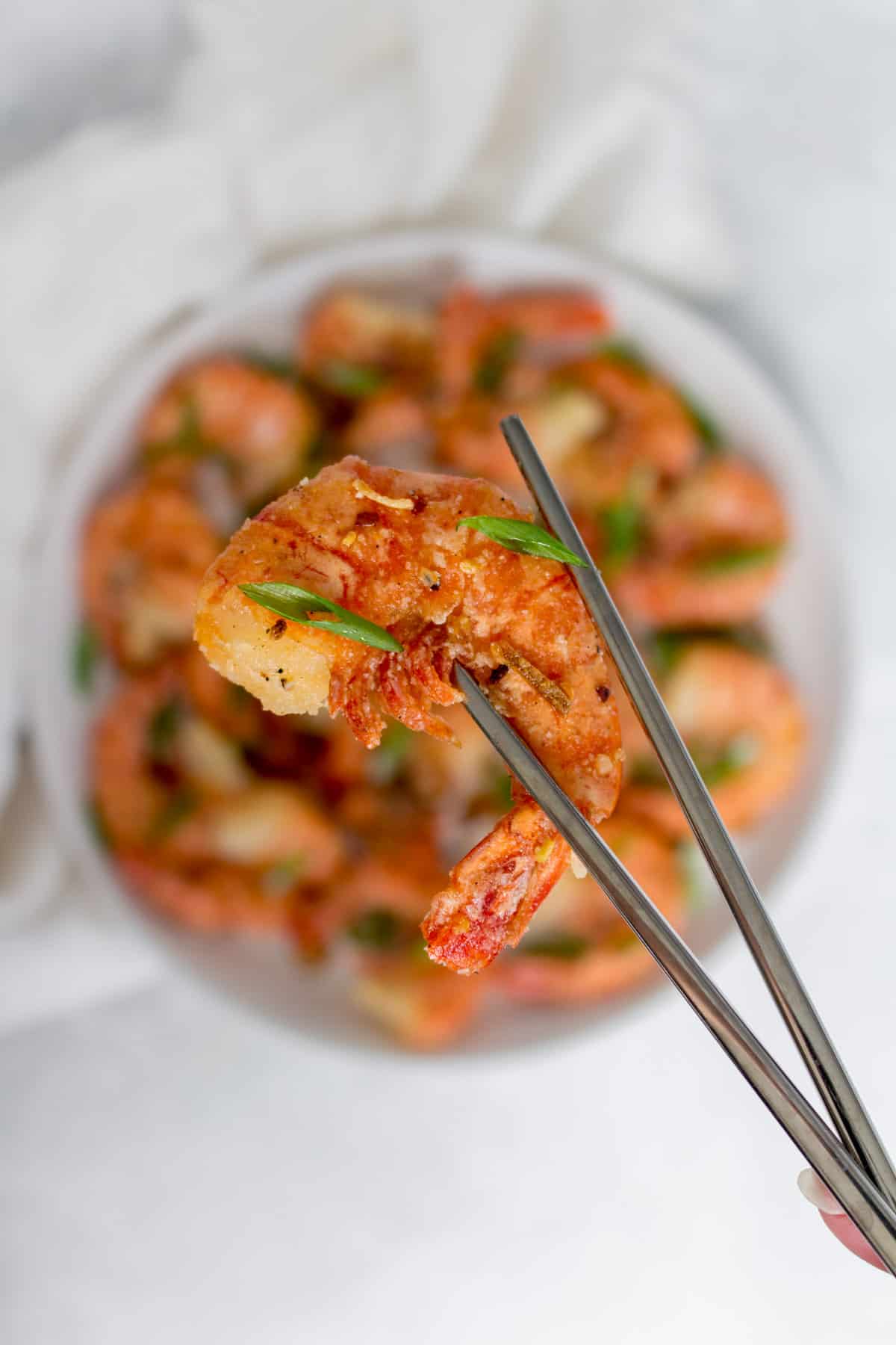 Chop stick holding up a single salt and pepper shrimp.