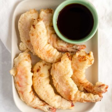 A platter of shrimp tempura with a bowl of dipping sauce.