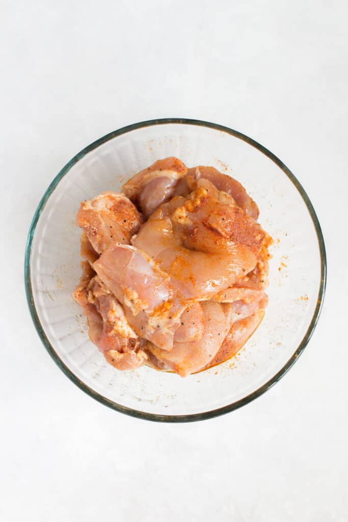 Chicken thighs in a bowl, seasoned.