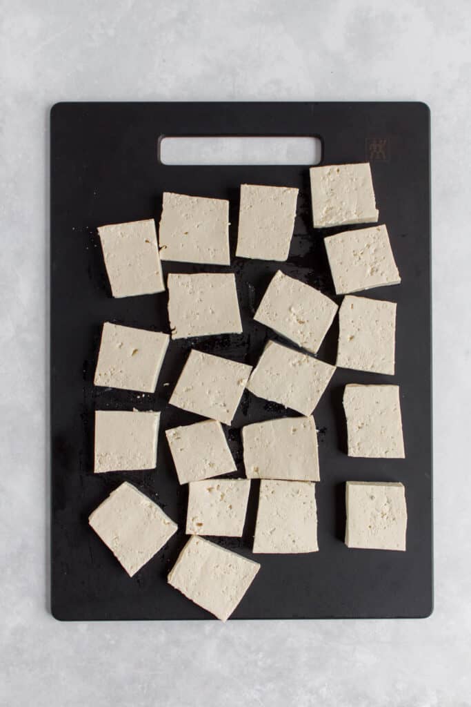 Tofu cut into squares on a cutting board.