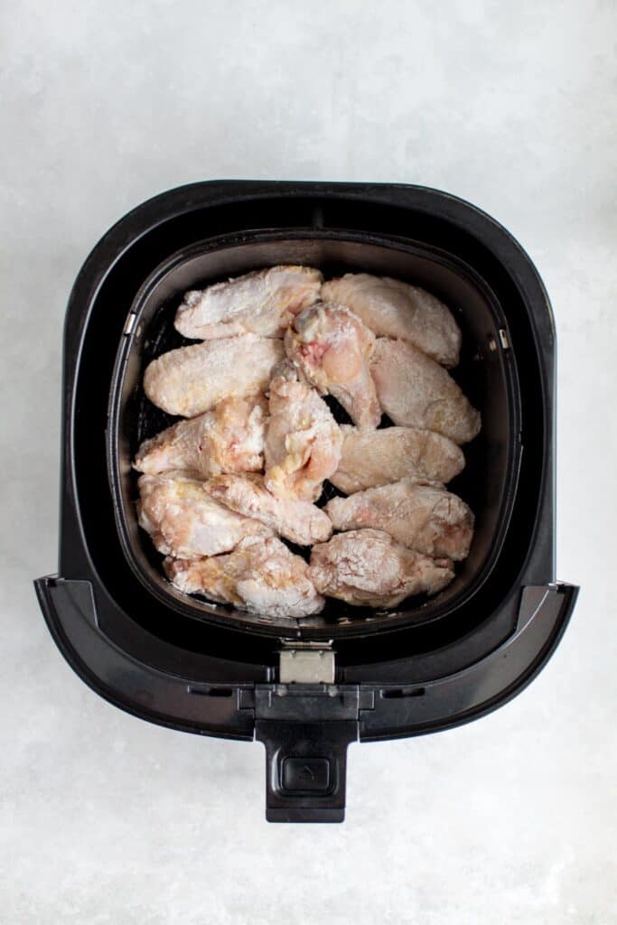 Air fryer basket with chicken wings.
