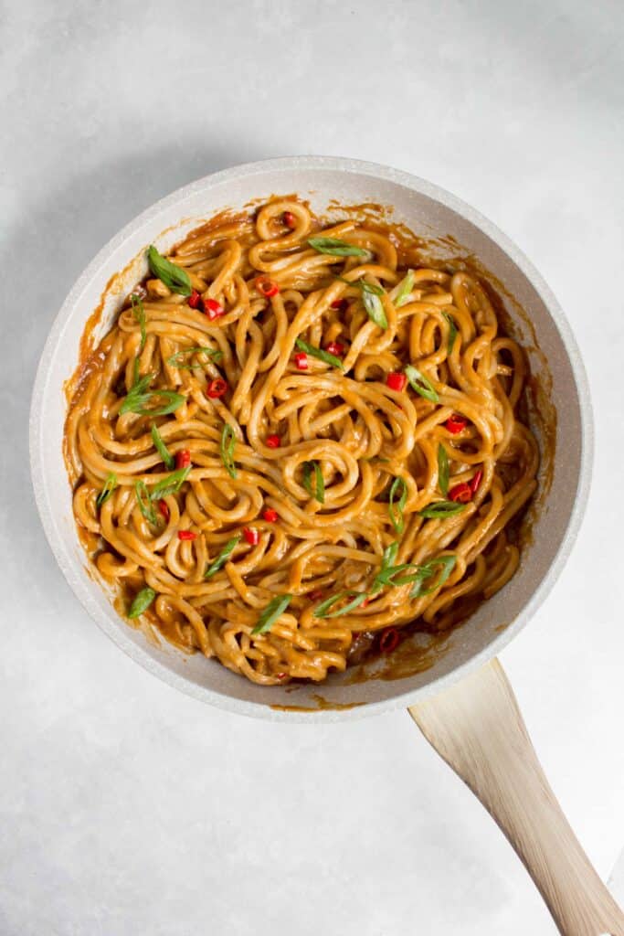 Spicy peanut udon noodles in a pan with green onions and red thai chili peppers on top.