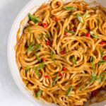 Spicy peanut noodles in a pan with green onions and red thai chili peppers on top.