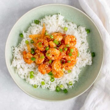 Overhead view of a plate of rice with sweet and spicy shrimp on top.