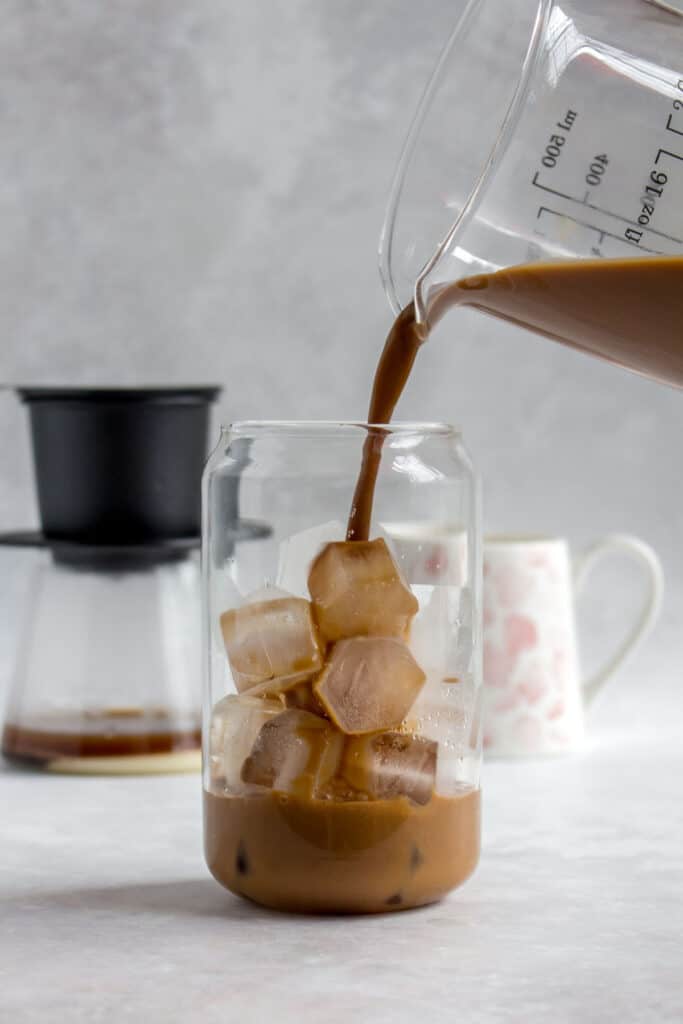 A glass of Vietnamese coffee being poured into a glass of ice.