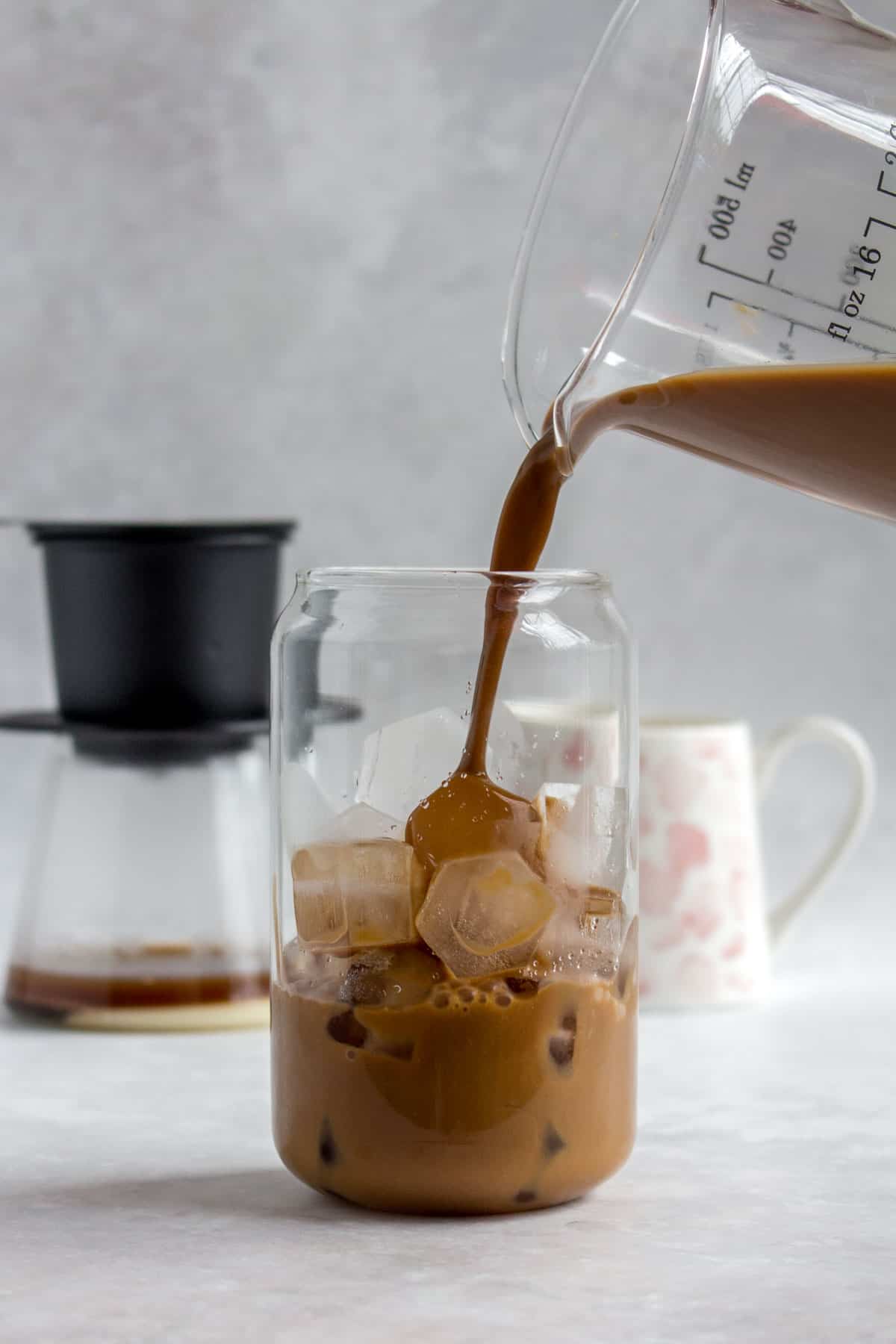 A glass of Vietnamese coffee being poured into a glass of ice.
