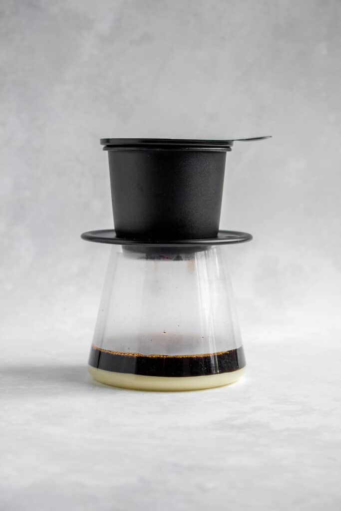 Glass with a Vietnamese coffee phin on top and coffee dripping in.