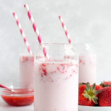Three glasses of strawberry milk with pink striped straws.