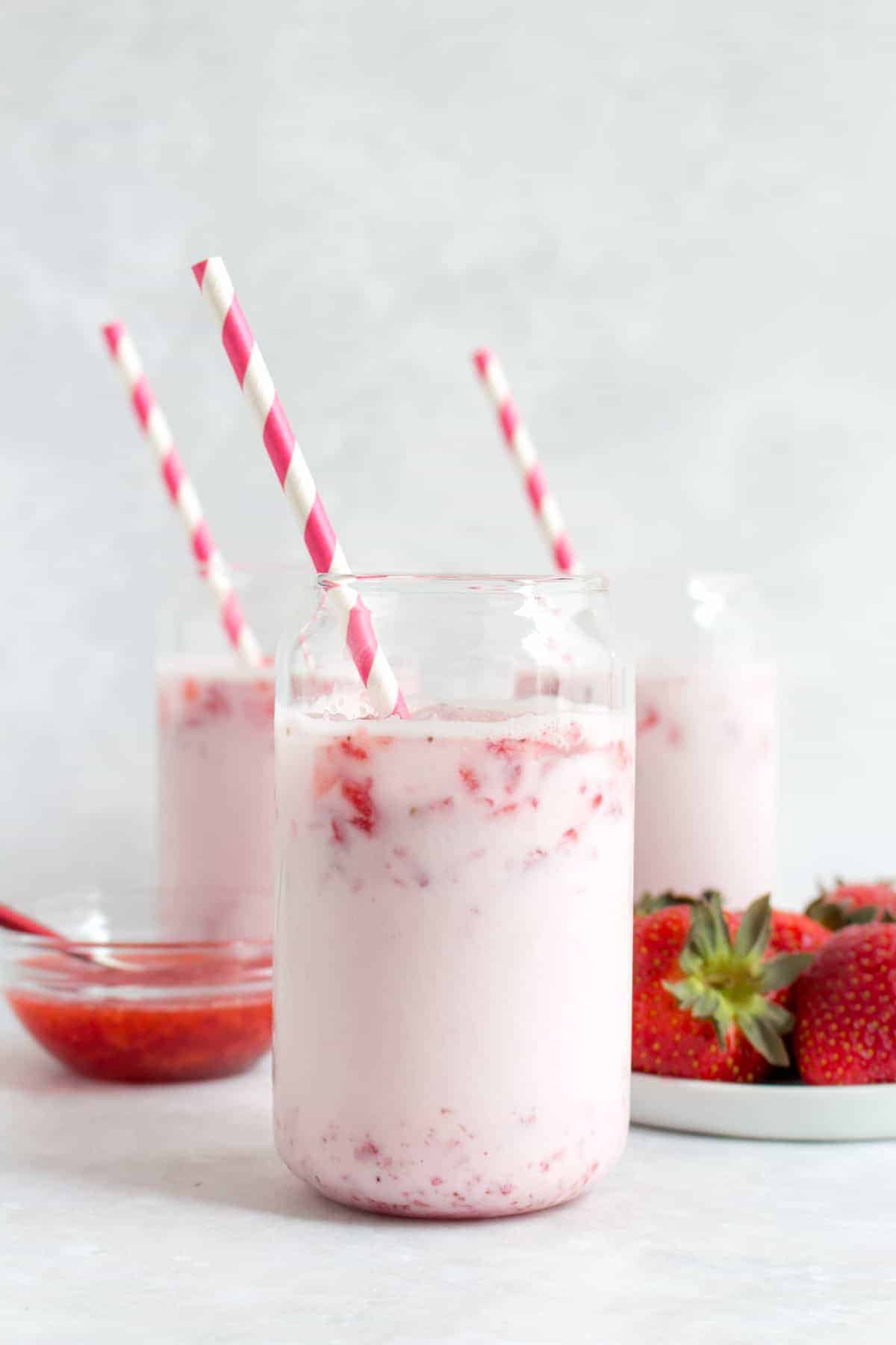 Three glasses of strawberry milk with pink striped straws.