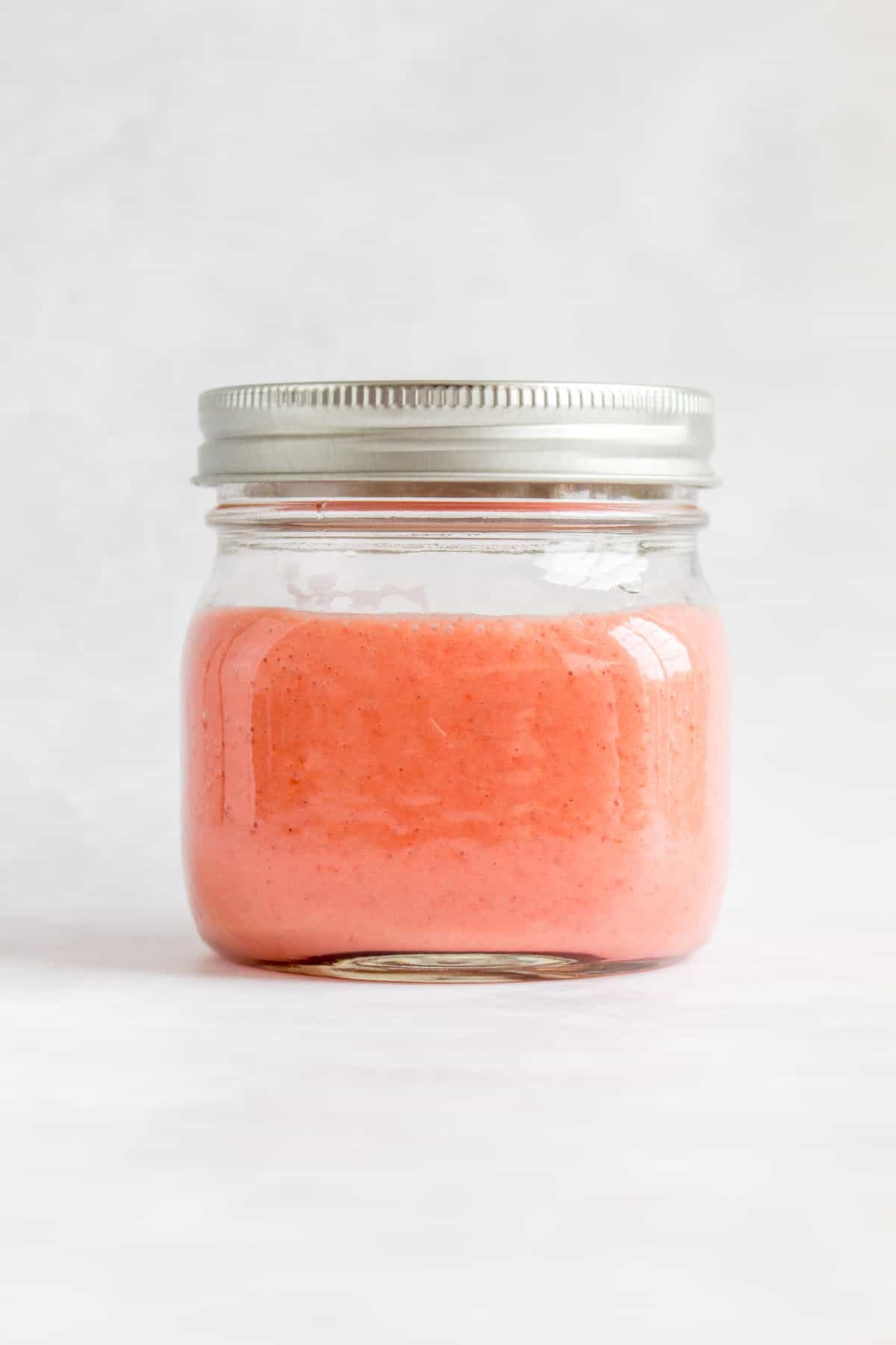 A mason jar with the lid on containing strawberry vinaigrette.