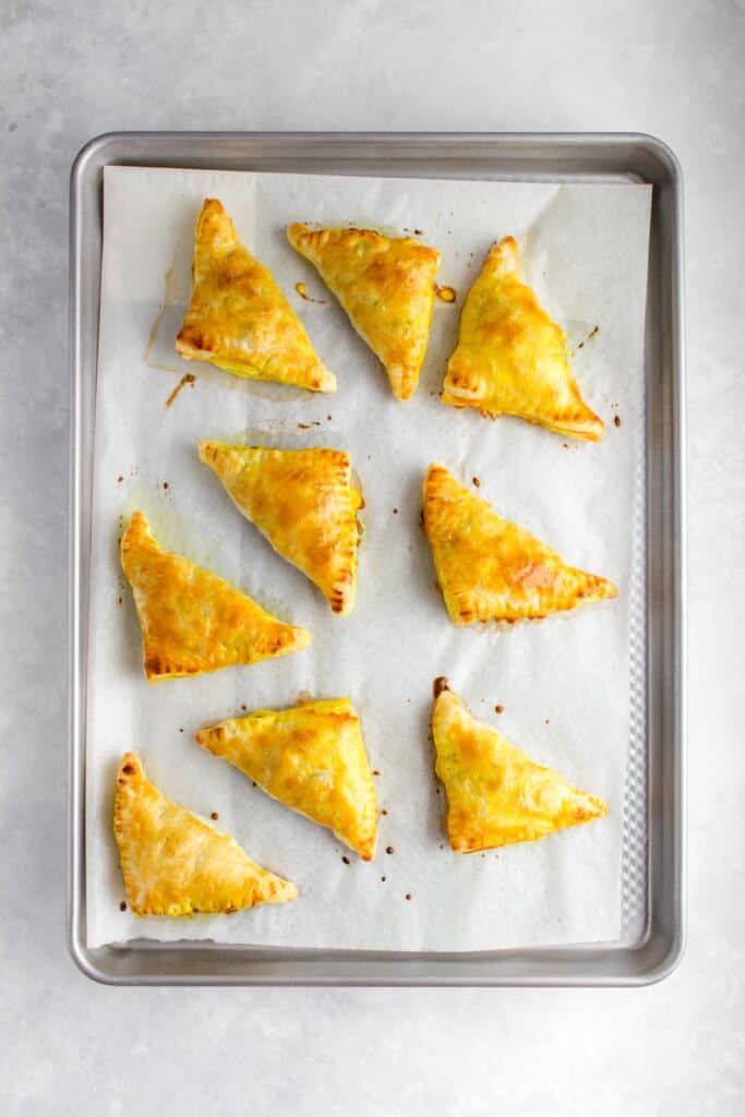 Beef curry puffs baked on a lined sheet pan.