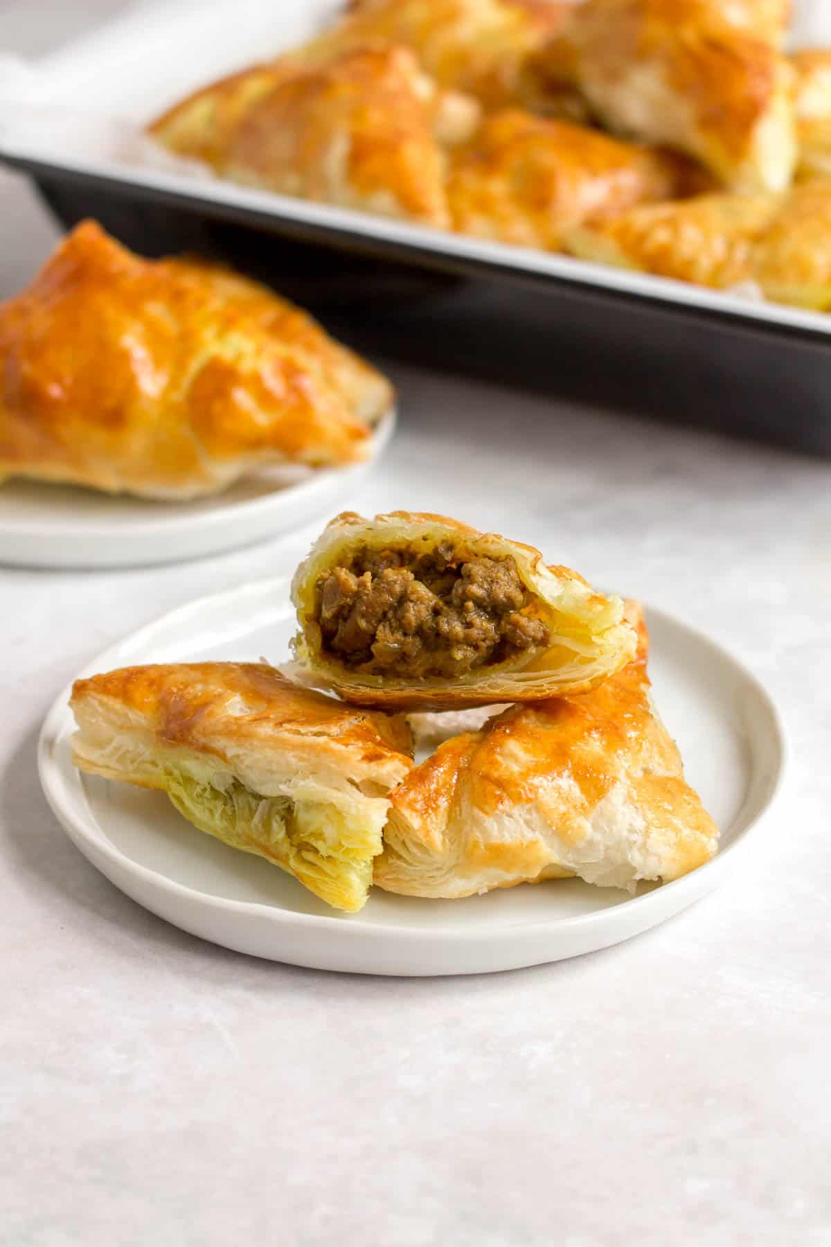 Beef curry puff cut in half, on top of two more on a plate.