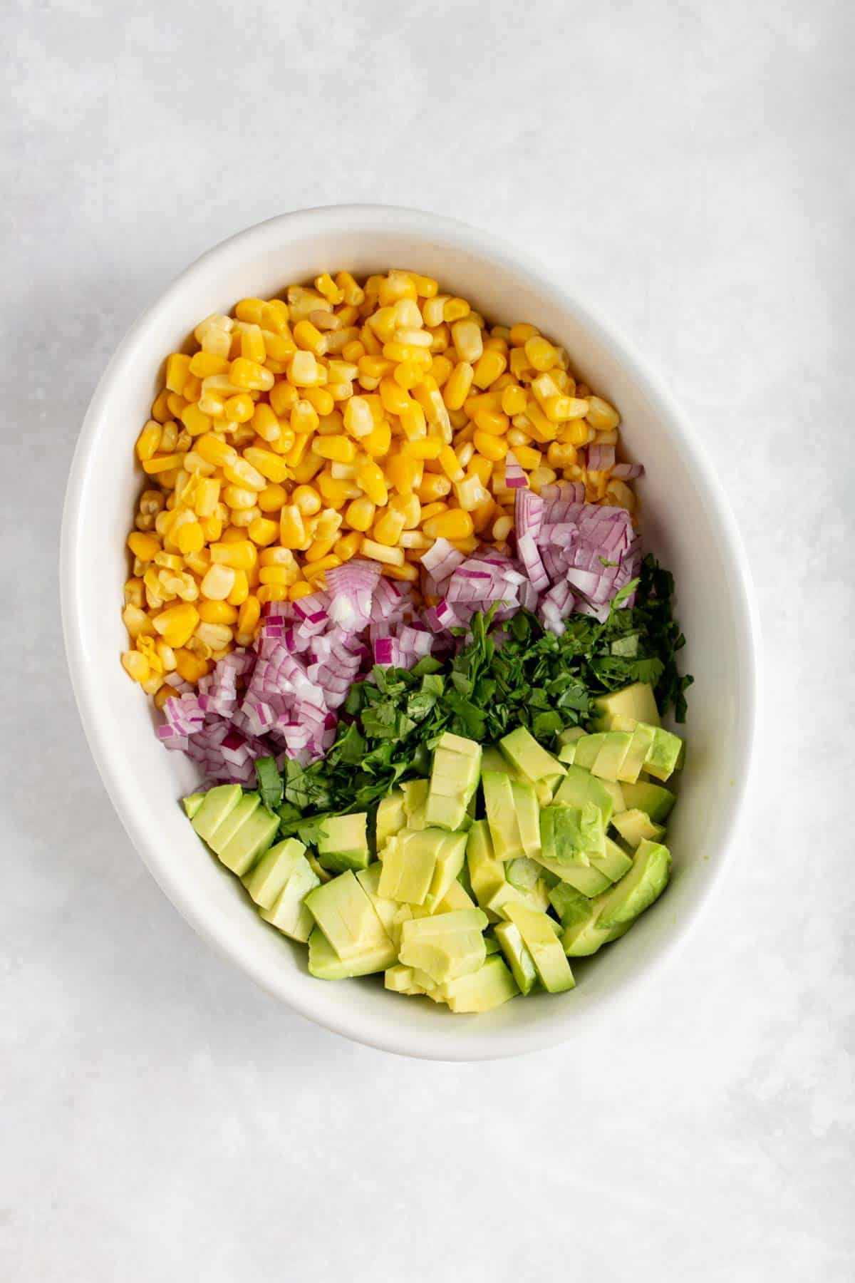 Overhead view of corn avocado salsa ingredients lined in a bowl.