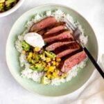 A steak bowl with flank steak, corn salsa, and sour cream with a fork in it.