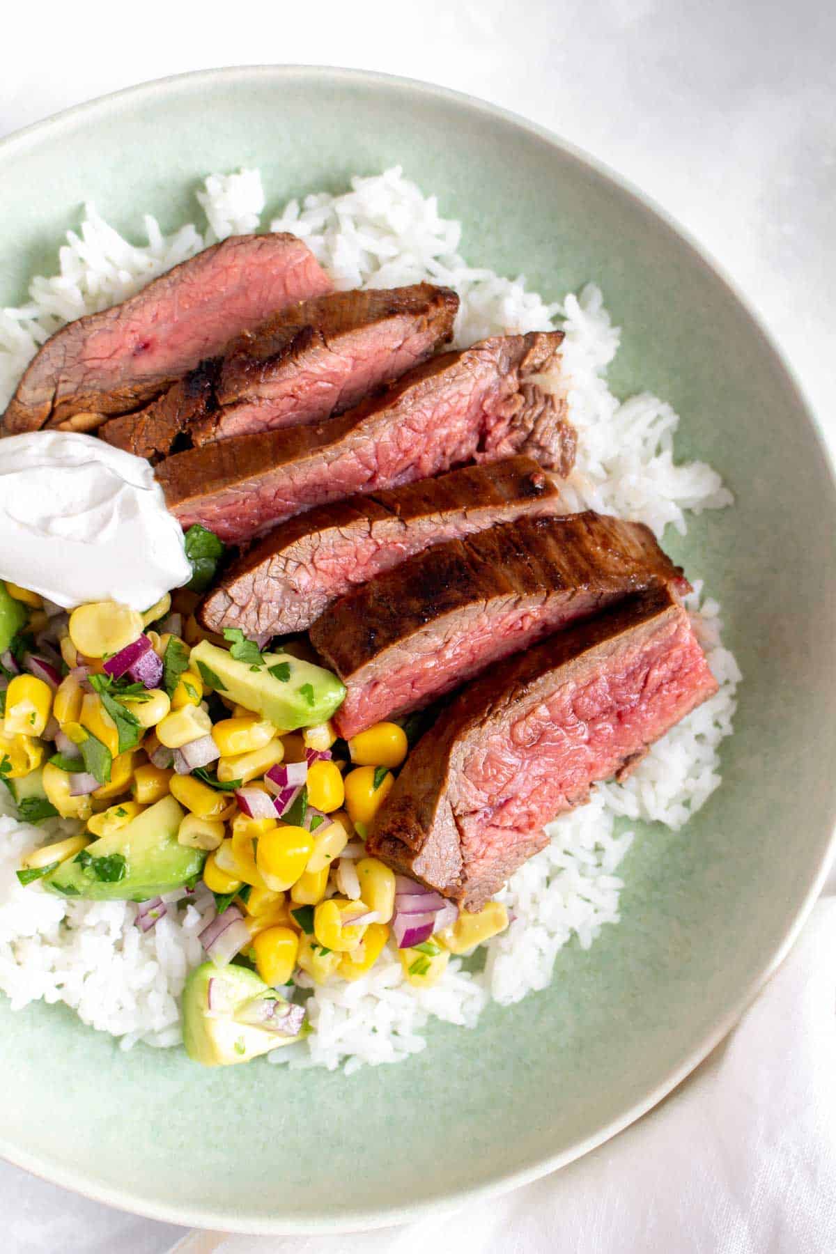 Close up of flank steak sliced over top of a bed of rice with corn salsa.
