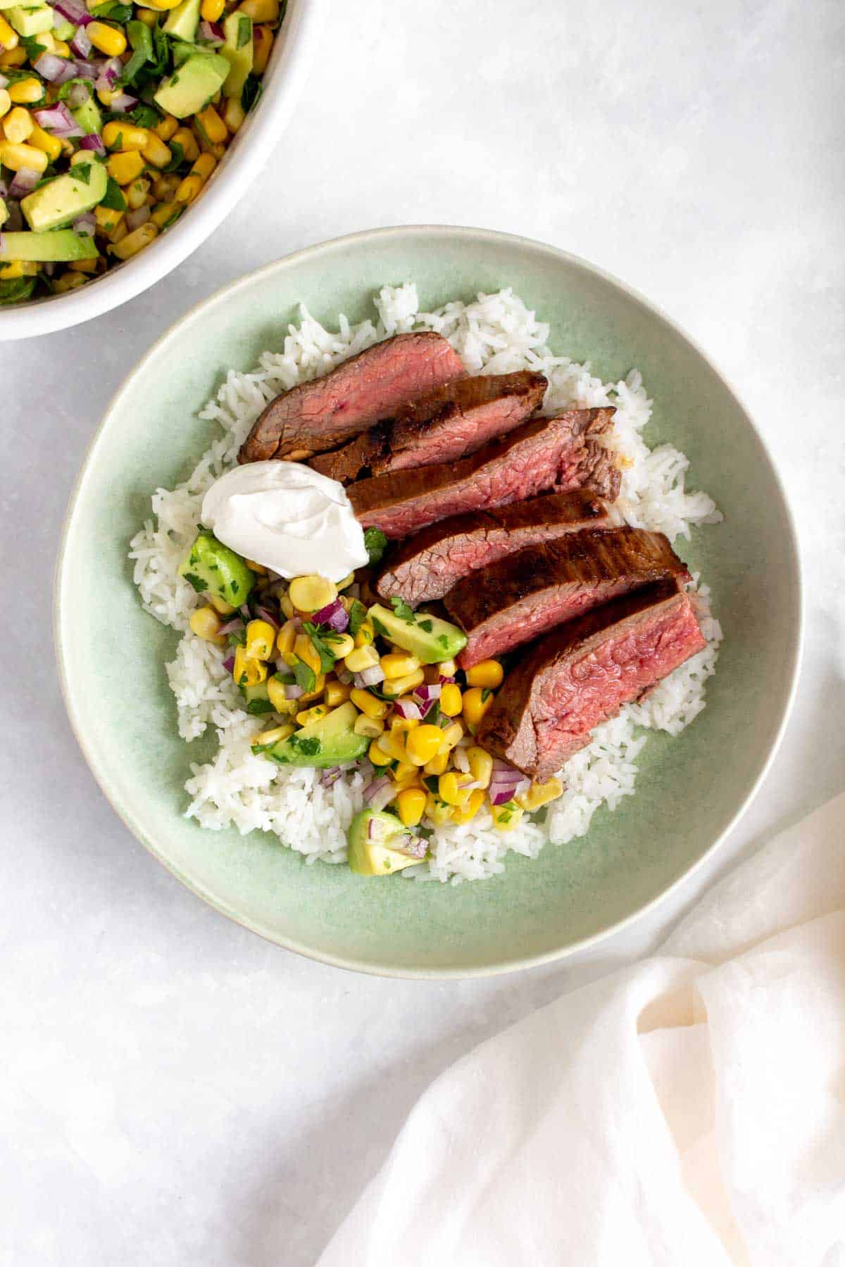 A bowl of rice with sliced steak with corn salsa and cream cheese.