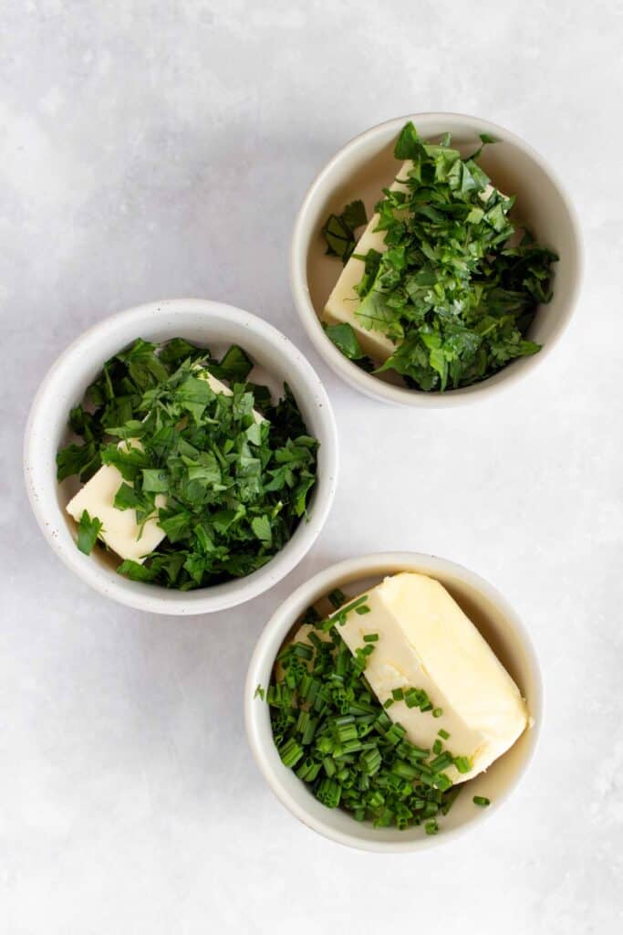 Three small bowls with butter and herbs.