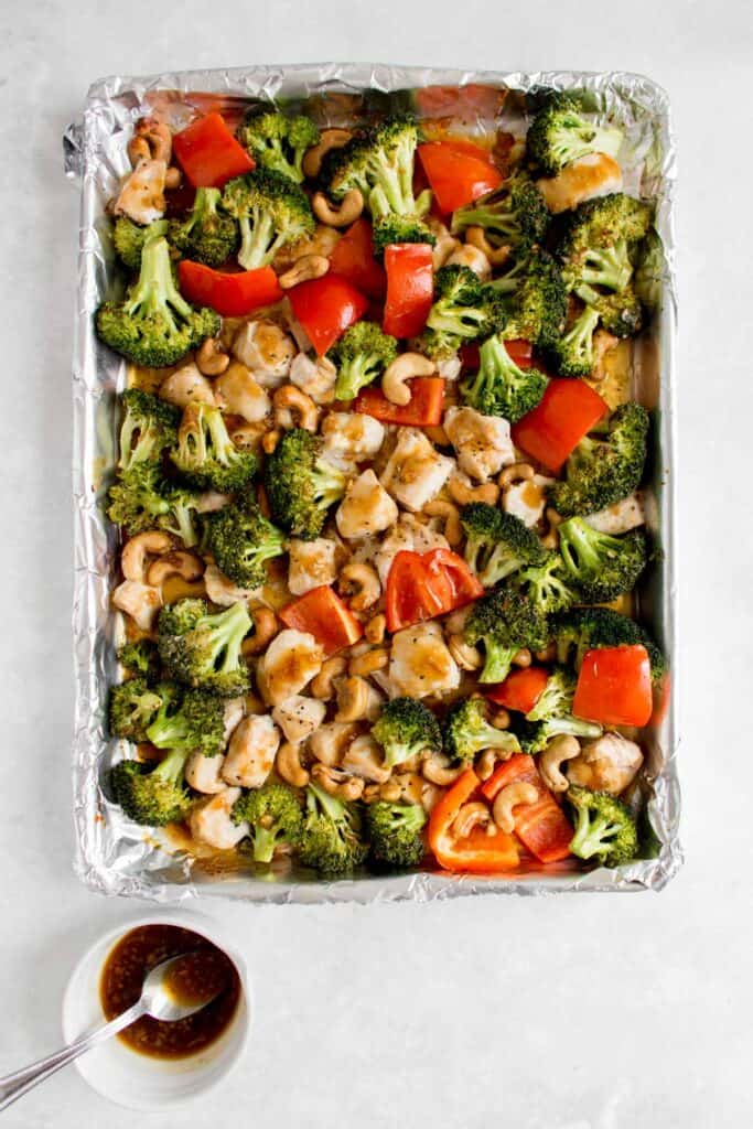 Sheet pan cashew chicken with sauce on the side to be drizzled onto the sheet pan.