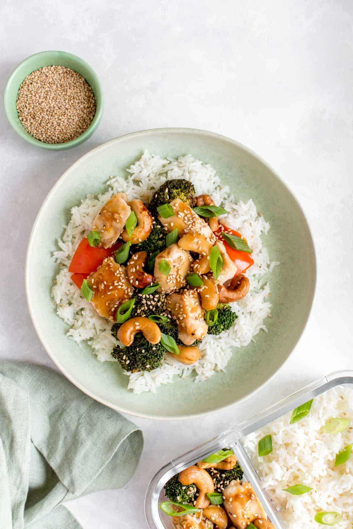 A plate of rice with cashew chicken on top with some sesame seeds on the side and as garnish.