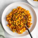 A plate of couscous salad with chorizo, corn, and chickpeas with a spoon.