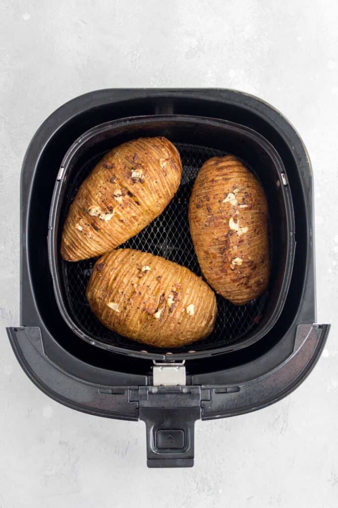 Air fryer basket with cooked air fryer hasselback potatoes.