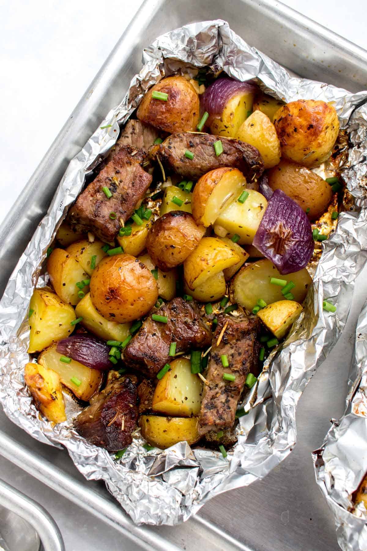 Overhead view of a packet of steak and potatoes, opened, on a half sheet pan.