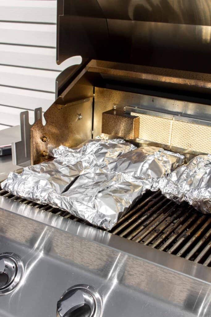 Four steak and potatoes foil packet on a grill.