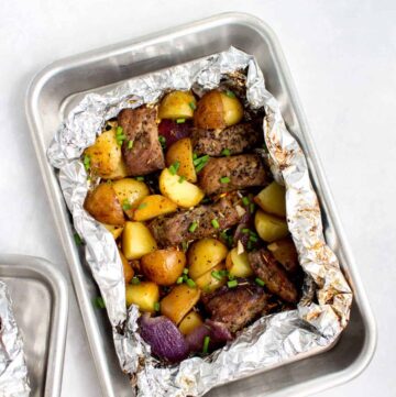 A steak and potatoes foil packet opened on a quarter sheet pan.