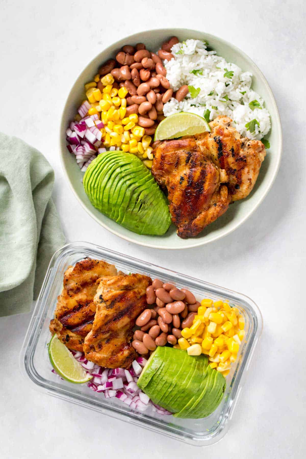 Meal prep container and a plate each with grilled cilantro lime chicken thighs, corn, pinto beans, red onions, sliced avocado, and a wedge of lime.