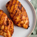 Close up of one of two grilled chicken breasts on a plate.