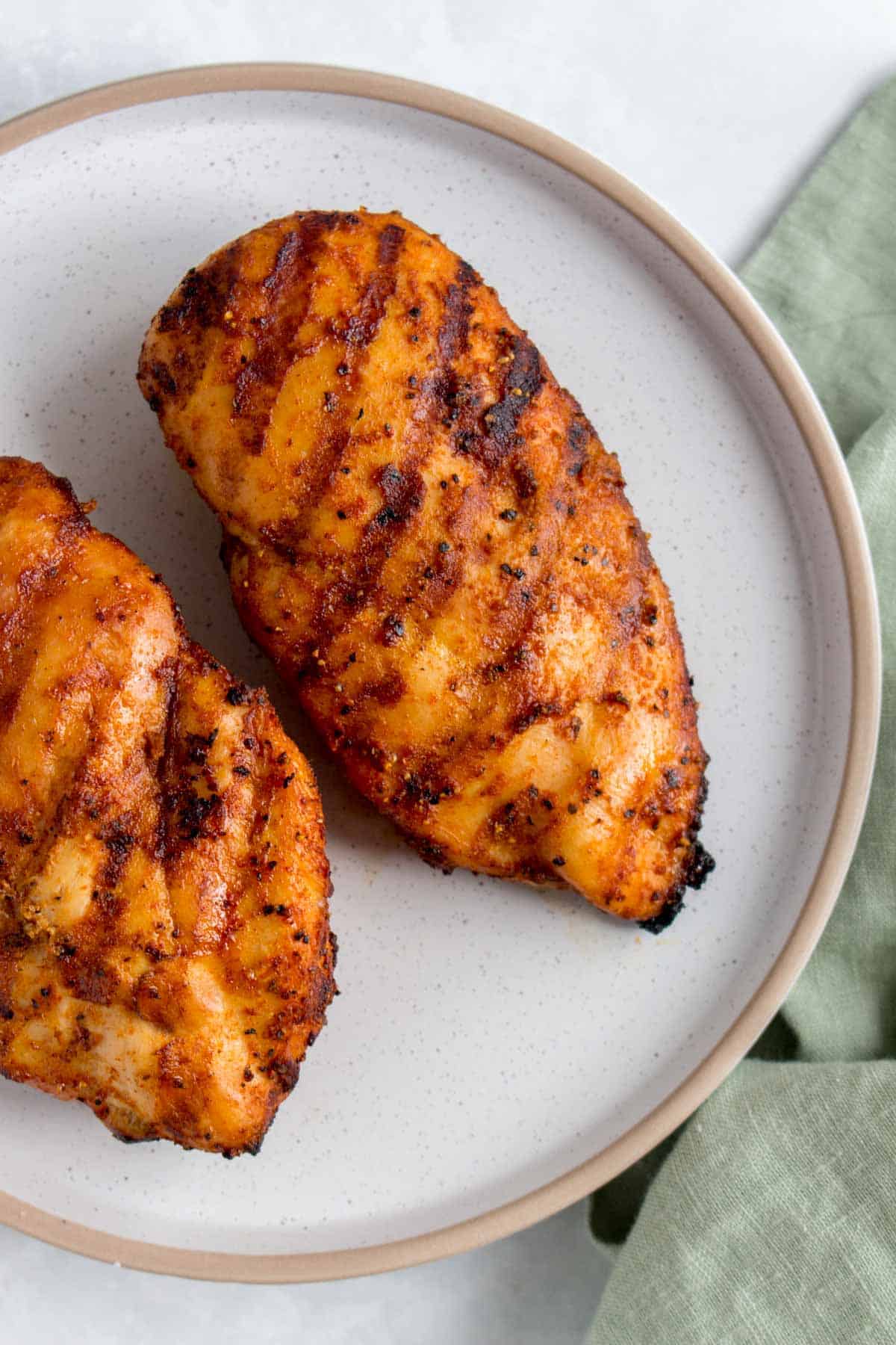 Close up of one of two grilled chicken breasts on a plate.