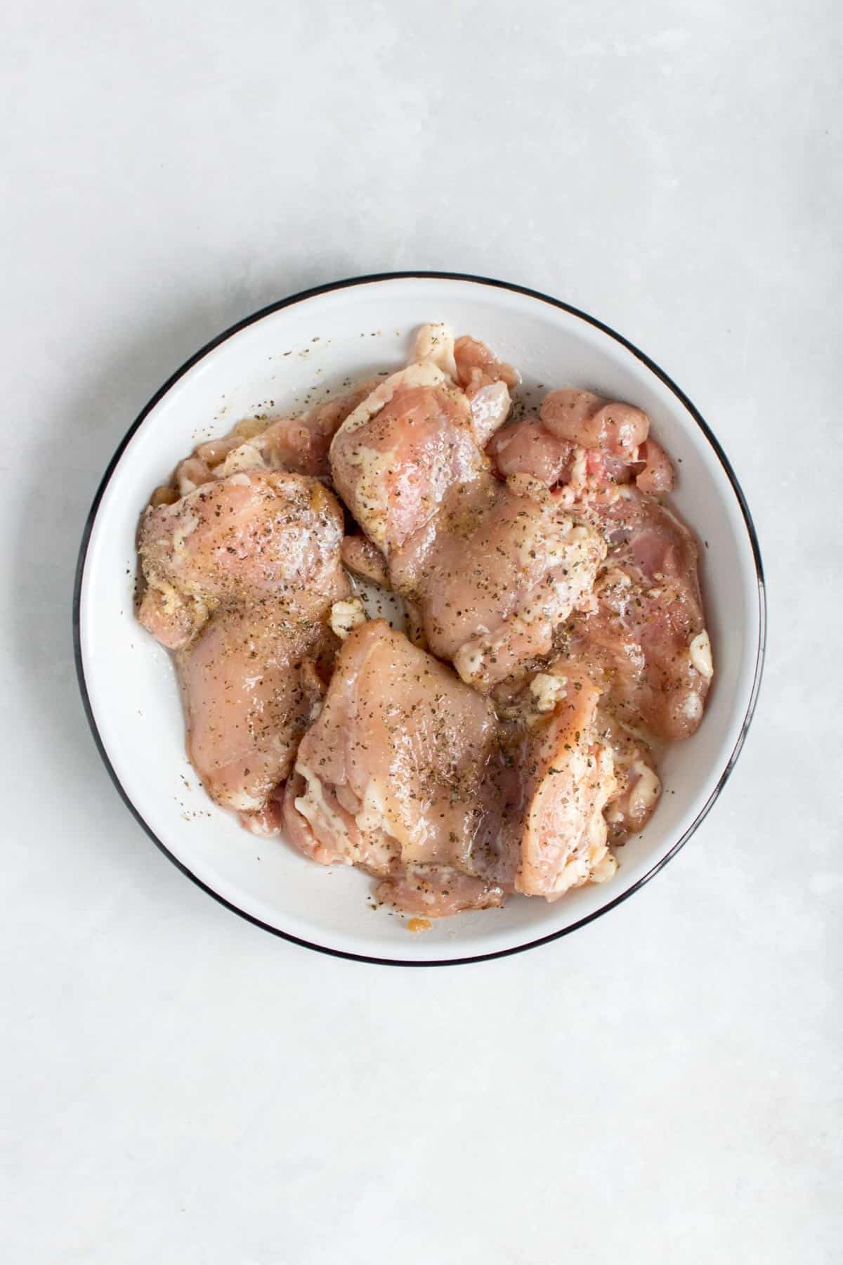 Chicken thighs, seasoned, in a plate.