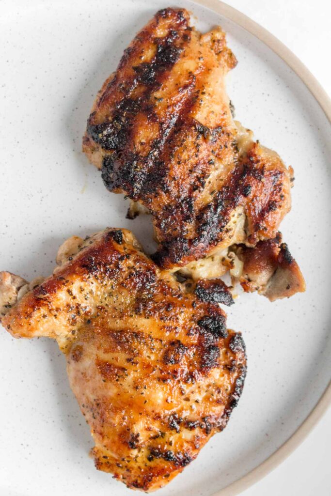 Close up of two grilled chicken thighs on a plate.