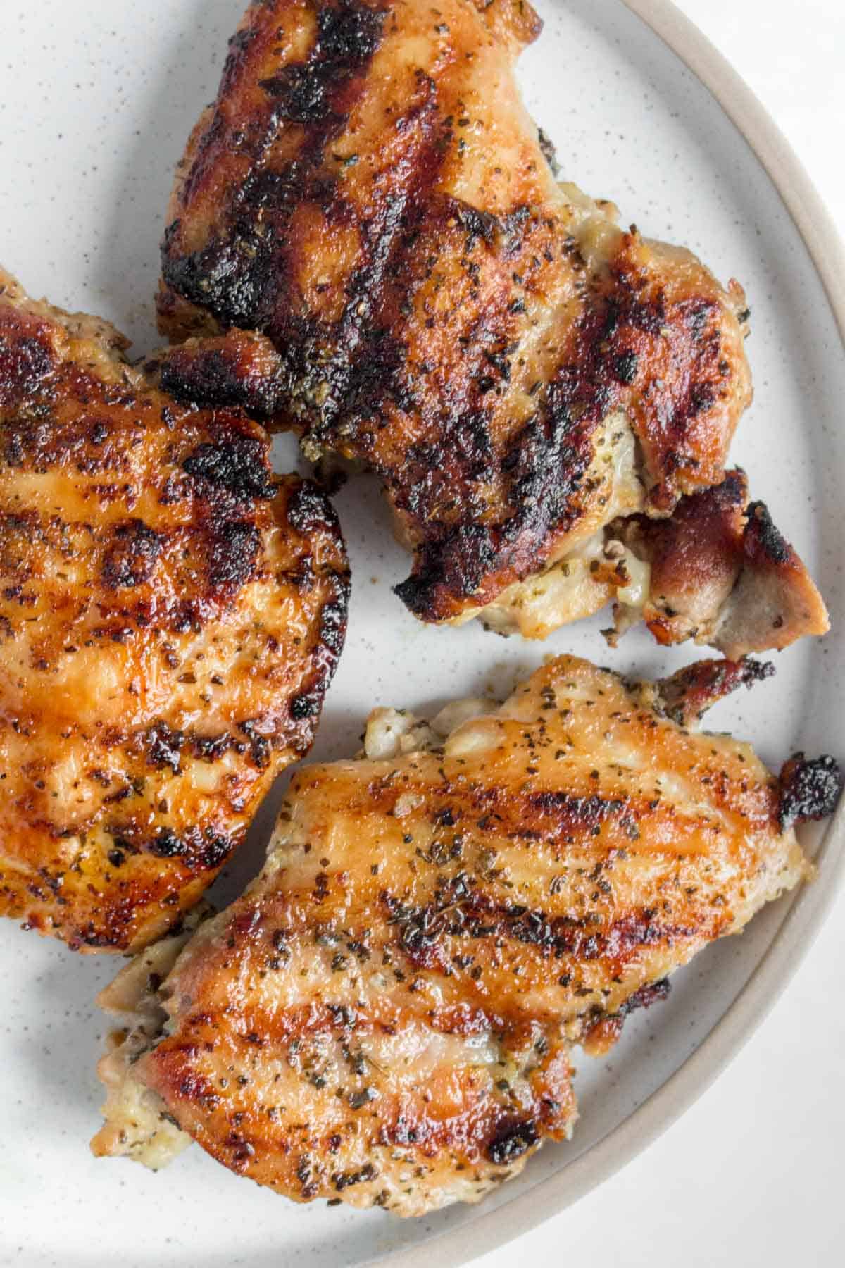 Close up of three grilled chicken thighs on a plate.