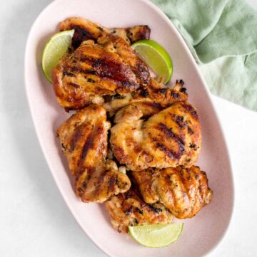 A pink platter of cilantro lime grilled chicken thighs with lime wedges.