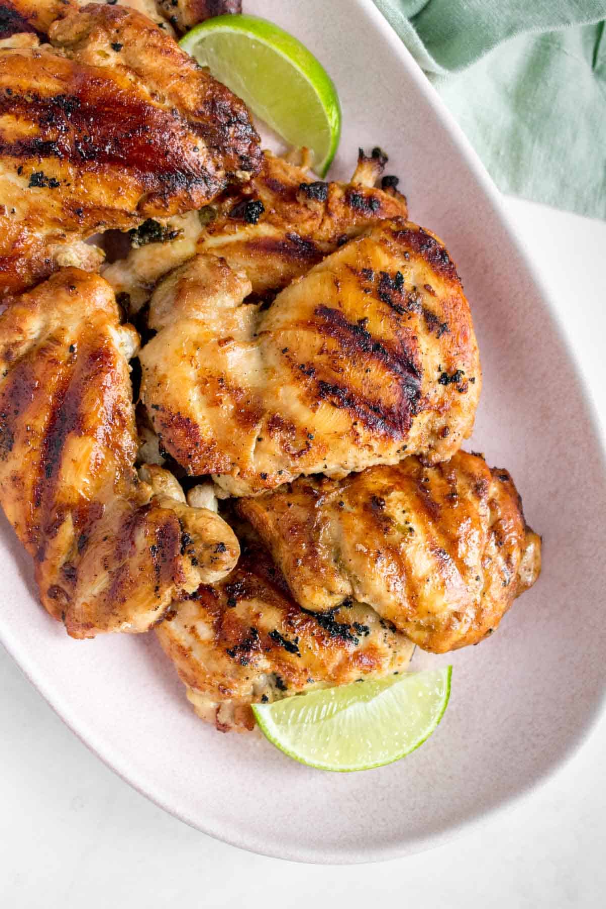 Close up of a pink platter of grilled cilantro lime chicken thighs with lime wedges.