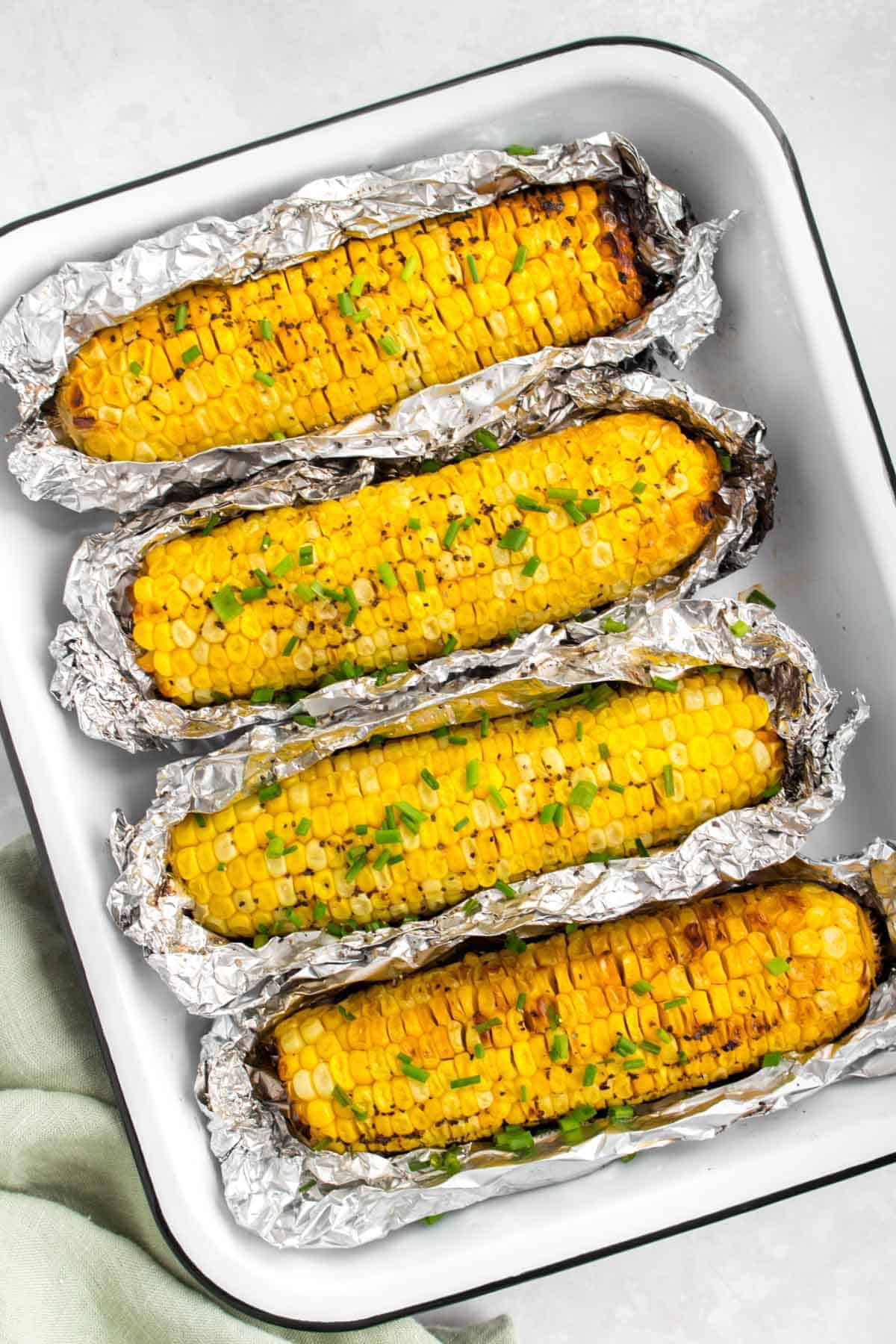 Overhead view of a tray with four corn on the cob with tin foil around them.