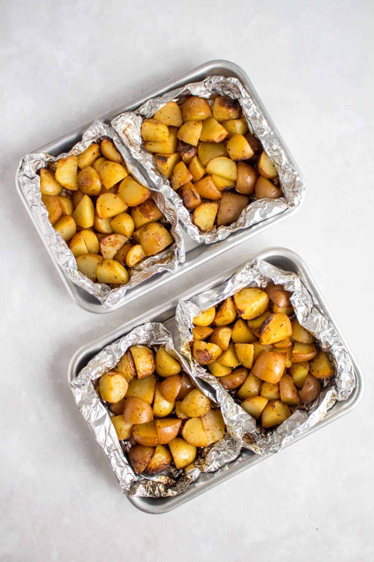 Overhead view of four foil packet potatoes on two sheet pans.