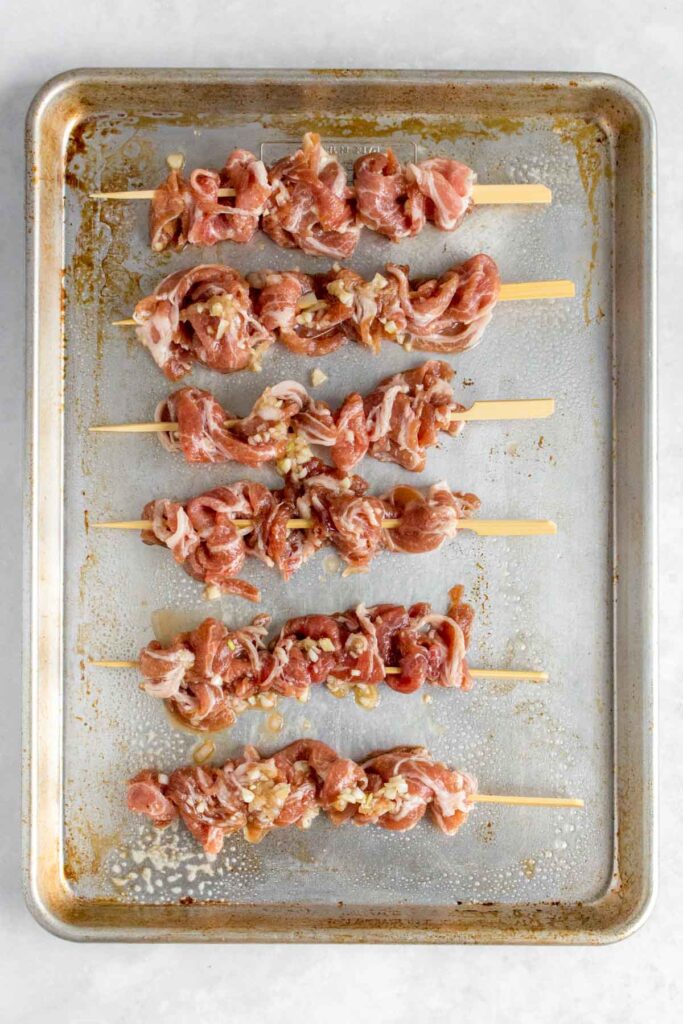 A sheet pan with pork on skewers.