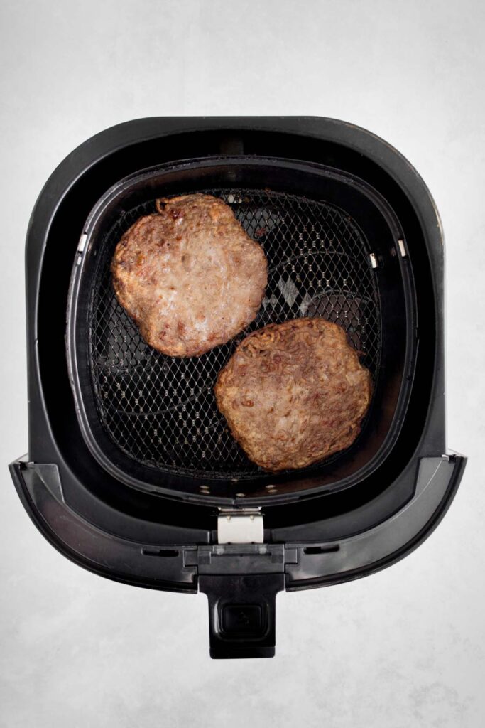 Two hamburger patties cooked in the air fryer basket.