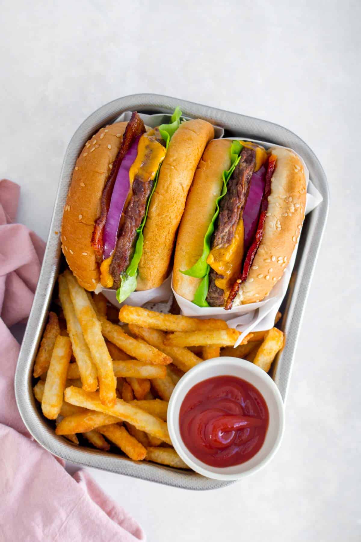 Two air fryer cheeseburgers in a serving tray with fries and ketchup.