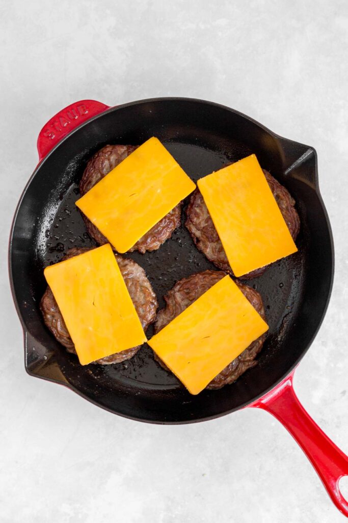 Cheese added to burger patties in a skillet.