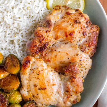 A plate with rice, Greek chicken thighs, and roasted Brussels sprouts.