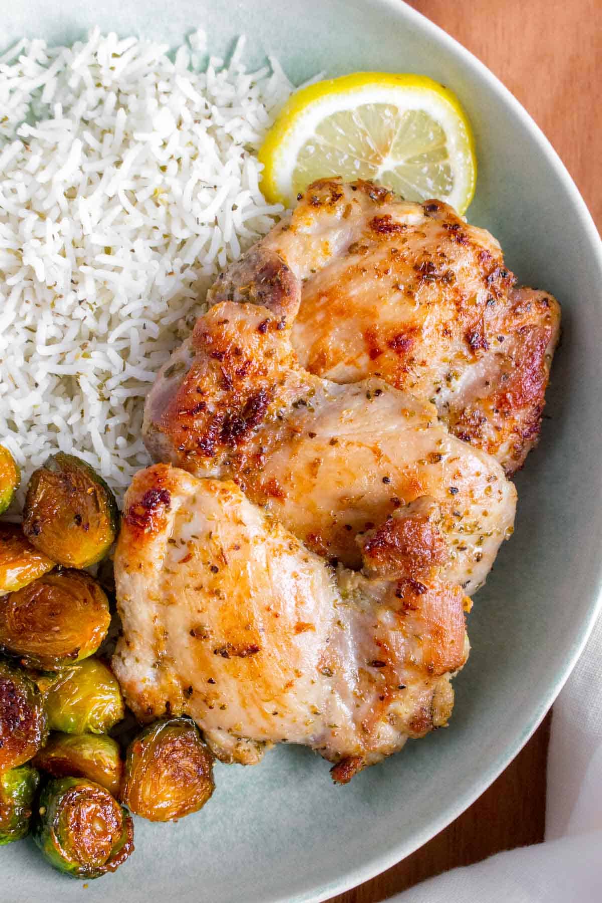 A plate with rice, Greek chicken thighs, and roasted Brussels sprouts.