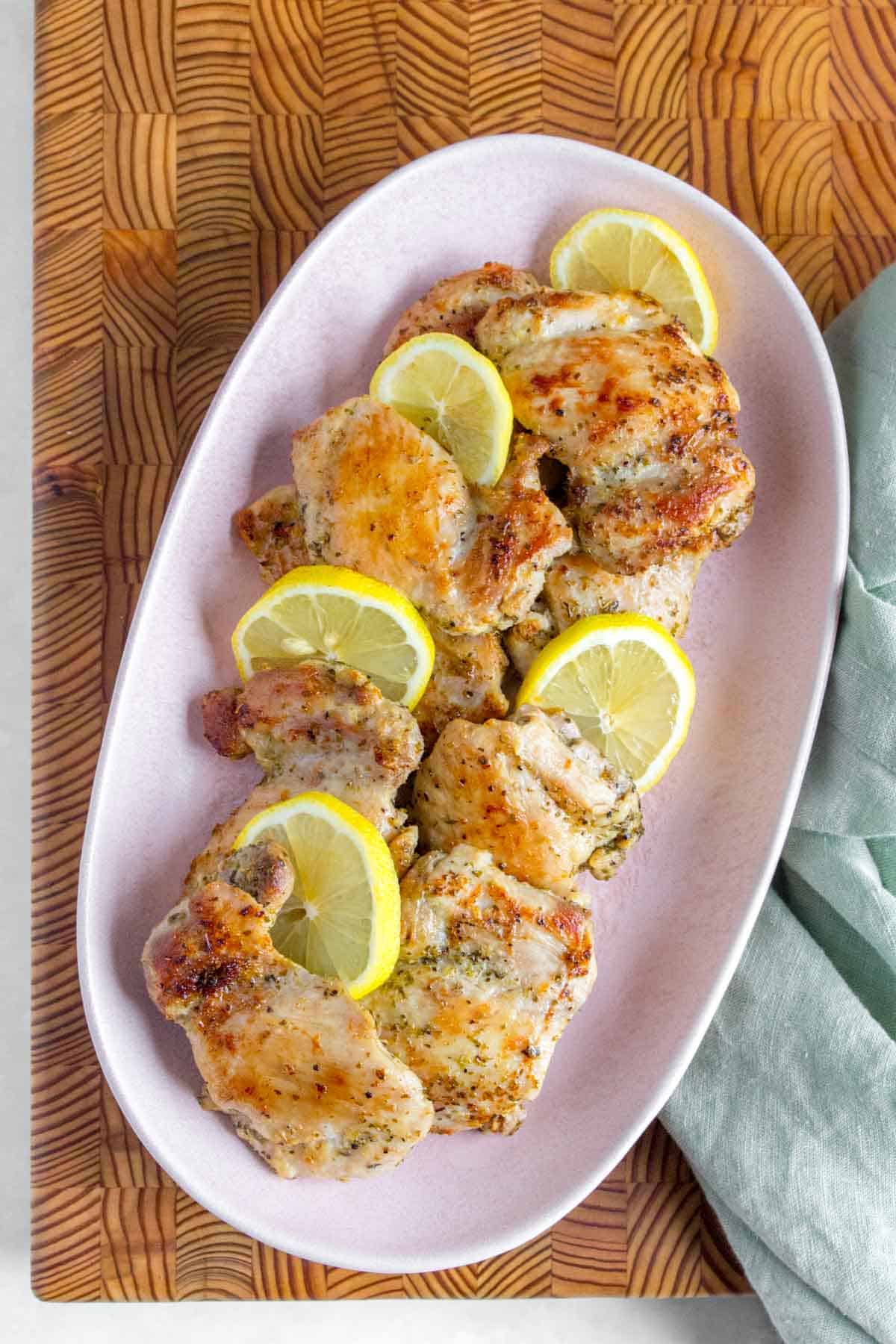 A platter of Greek chicken thighs with sliced lemons.
