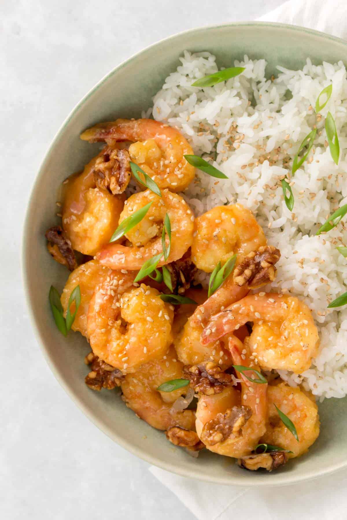 A bowl of honey walnut shrimp with rice, sesame seeds, and green onions.