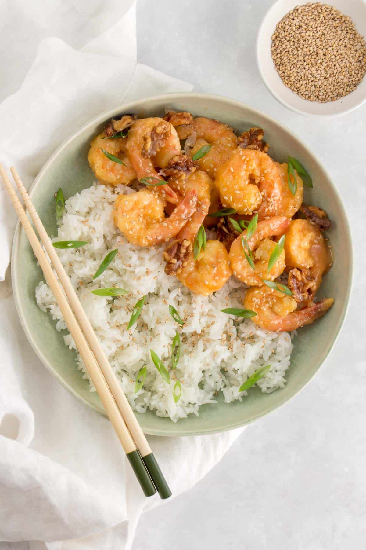 A bowl of rice with honey walnut shrimp with a pair of chopsticks.