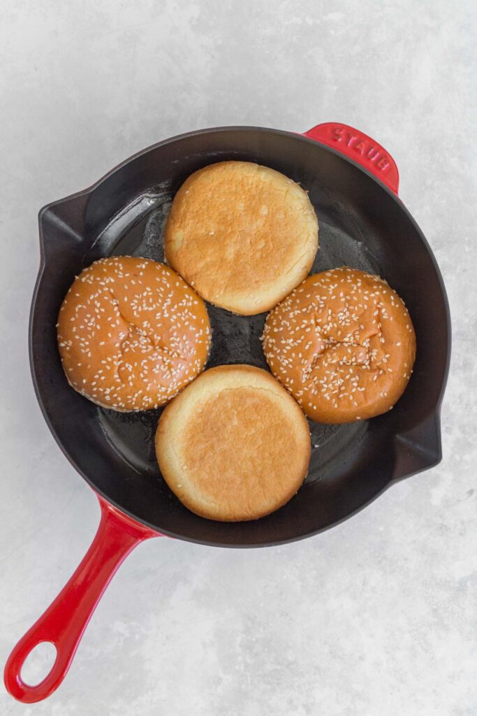 Burger buns toasting in a pan.