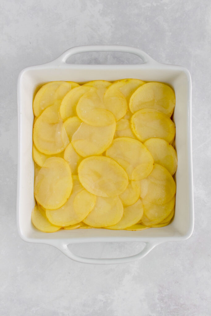 Sliced potatoes added to a baking dish.