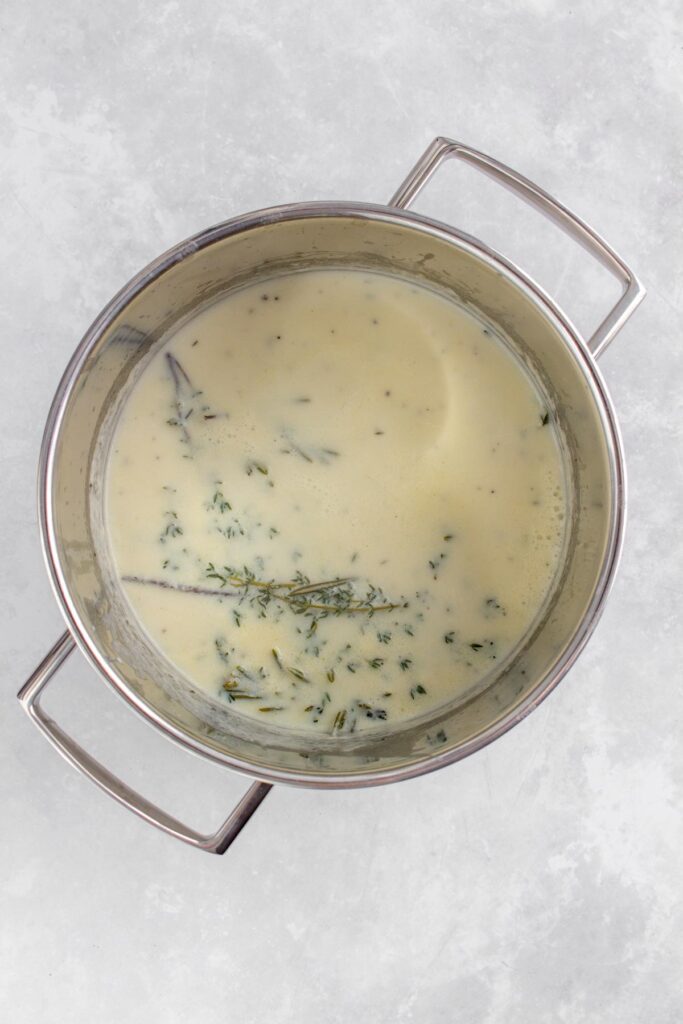 White sauce with herbs infused in a pot.